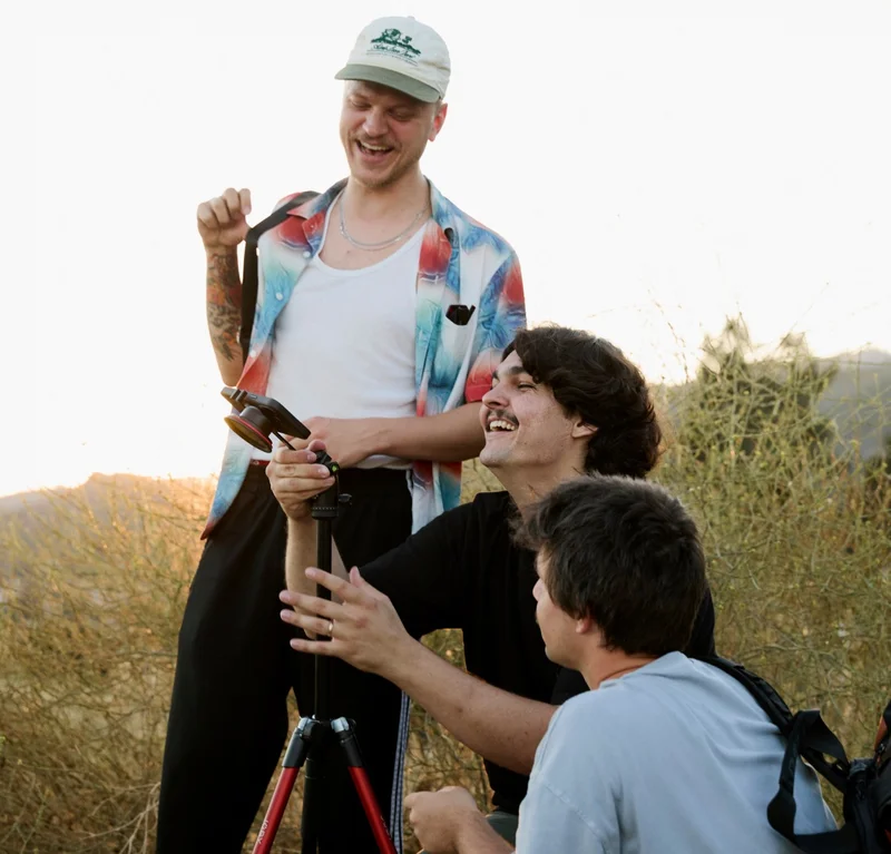 3 men looking at a phone on a tripod and laughing
