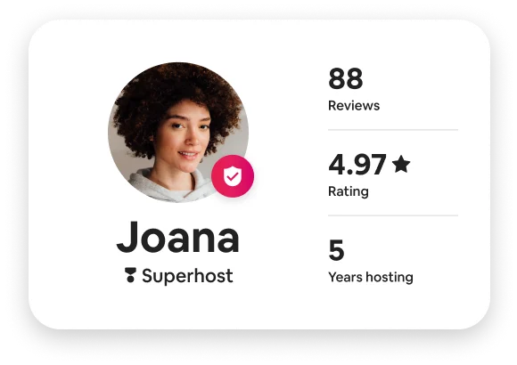 A circular profile picture of a woman with thick, dark, curly hair. Overlapping is an icon of a badge with a check mark. Her name is Joana and she has the title of Superhost. Her profile shows 88 reviews with an average 4.97 stars. She’s been hosting for 5 years.