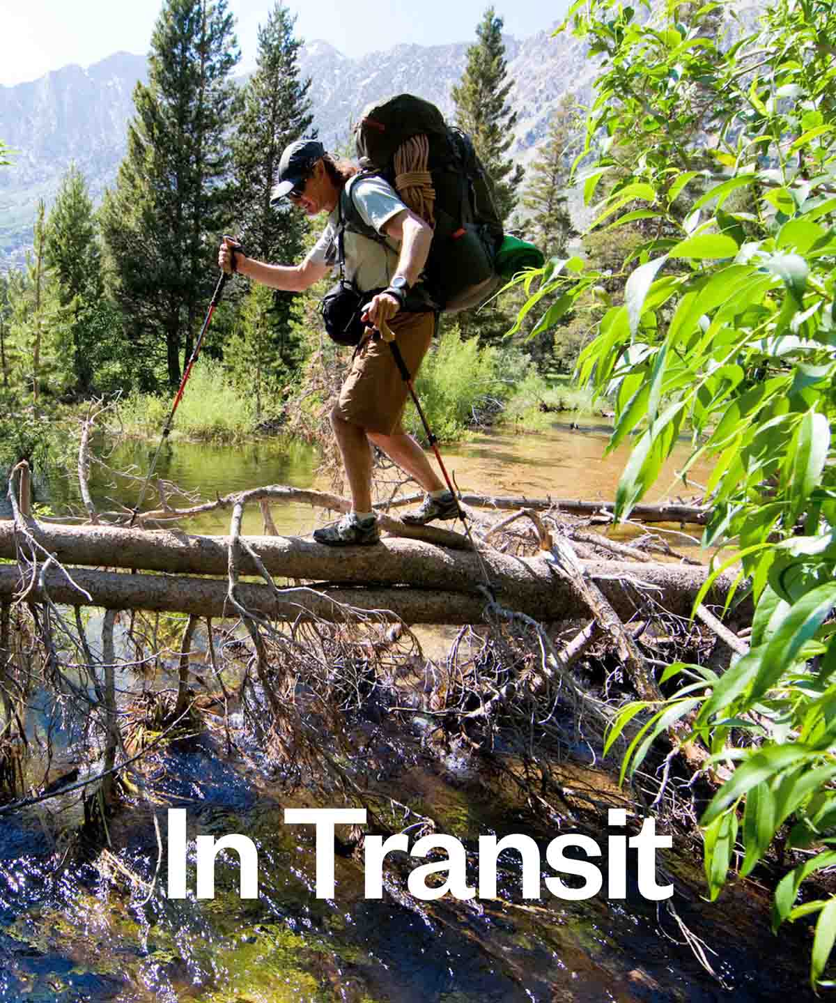 A backpacker walks over a fallen tree to cross a creek.