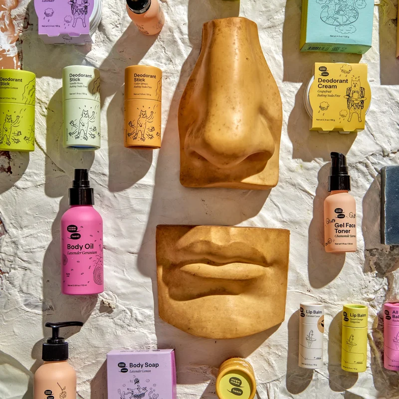 A flat lay of may skincare products in colorful packaging along with a giant nose and giant mouth.