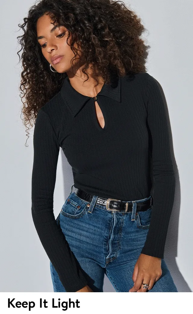 A woman wearing a black, long-sleeve top with blue jeans.