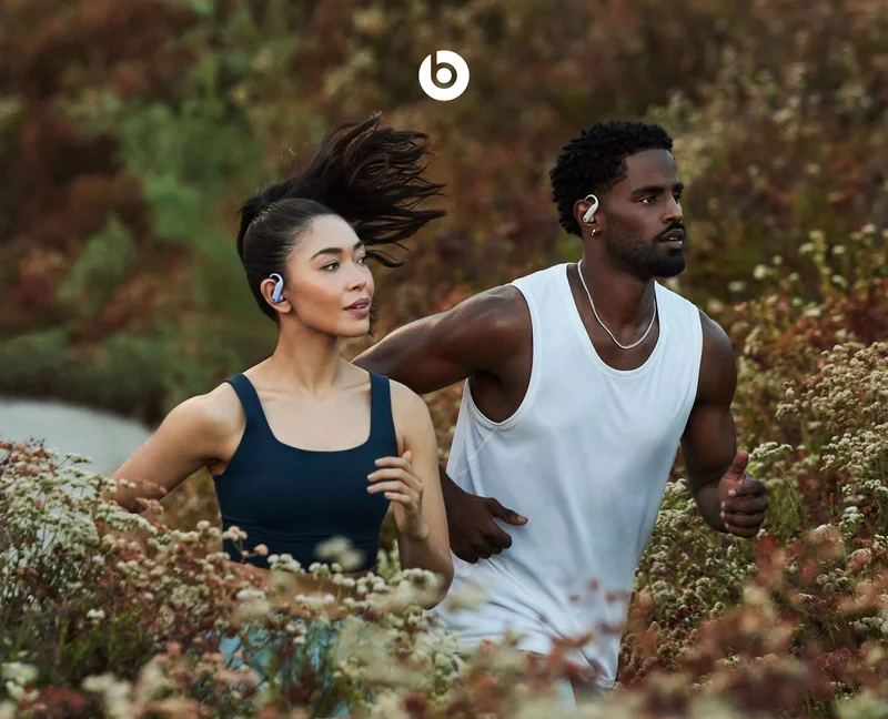 Woman and man running side by side using Powerbeats Pro 2 in Electric Orange.
