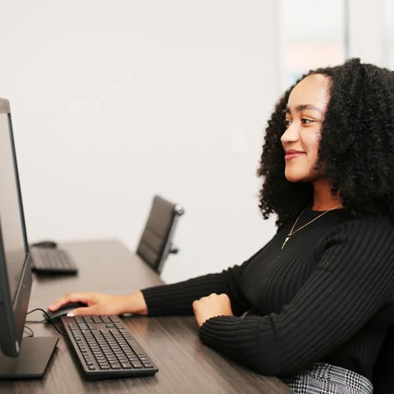 A woman with curly black hair sitting at a desk, using a computer.