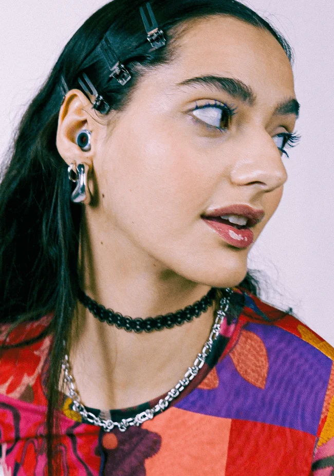 Woman dressed in a colorful retro outfit and Loop earplugs poses for the camera.