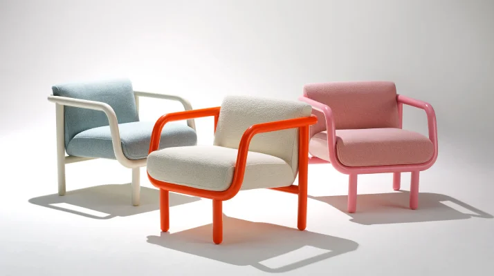 Three Percy lounge chairs are positioned together with a white background: orange frame and pink upholstery in the front, oyster frame and pale blue upholstery in the back left, and pale pink frame with pink upholstery in the back right.