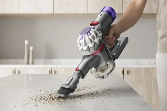 A Dyson Car+Boat handheld vacuum with the Combination tool cleans debris from a kitchen island.