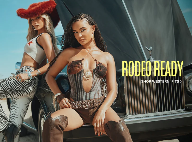 Two models rock rodeo-ready western fashion: a red fuzzy hat, zebra print pants, a corset top, and cowboy boots, posed by a classic car. Shop western fits.