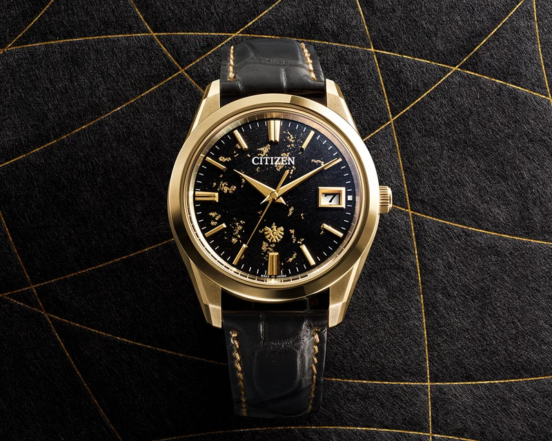 A close-up shot of The CITIZEN watch, with a black washi paper dial flecked in gold and silver flakes, dressed in a gold-tone Super Titanium™ case and a black crocodile strap
