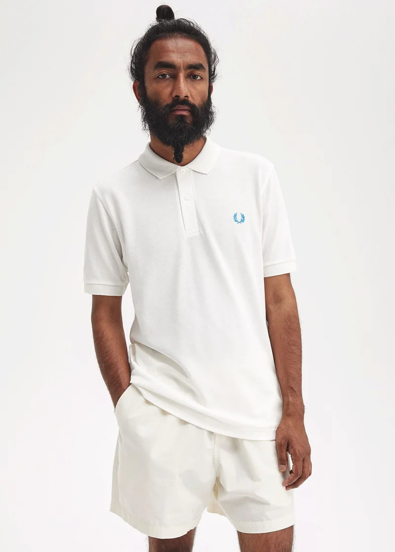 man wears a plain white Fred Perry Shirt with ocean blue laurel wreath logo