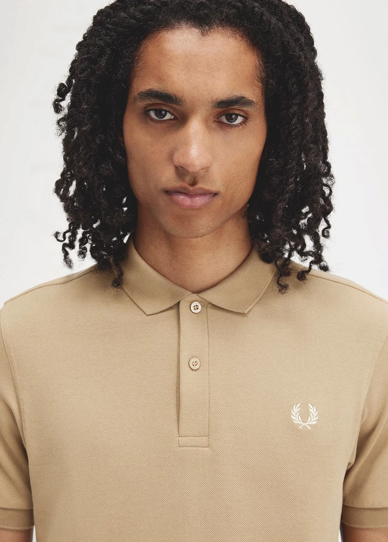 man wears the plain Fred Perry Shirt in a neutral tan colour