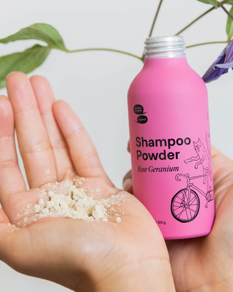 A tan set of hands shows some powder and a pink bottle of shampoo powder