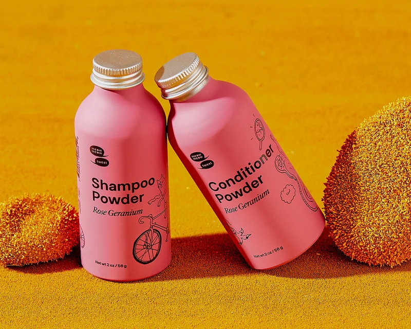 Two pink bottles sit propped on each other against a mustard background