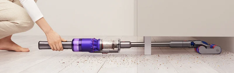 A woman cleaning under furniture with the Dyson Omni-Glide cordless vacuum