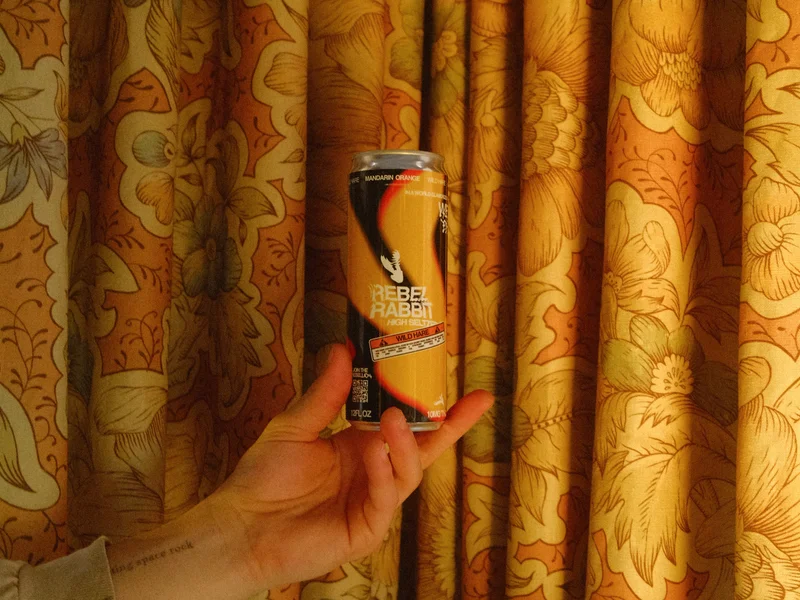 Someone hold a Wild Hare Mandarin Orange can in front on a curtain