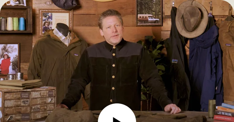 A person in a retail store holding a waxed cotton jacket.