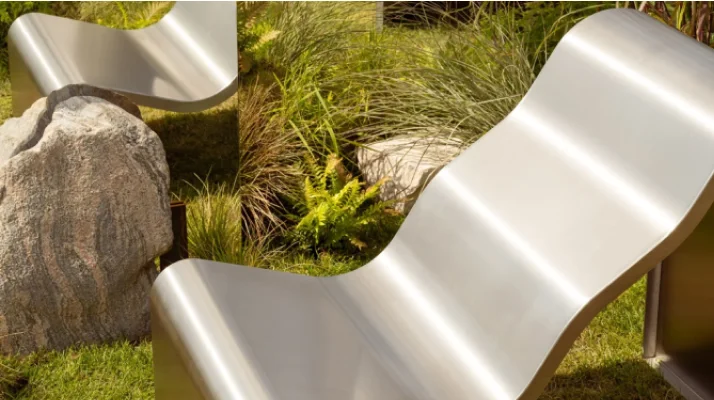 The Dream View Chair is placed on green grass, surrounded by lush plants. A nearby mirror reflects the chair, adding an intriguing touch to the outdoor arrangement.
