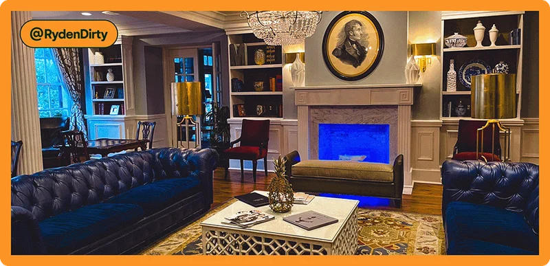 Image description: A living room with vintage furniture, blue couches, and a glowing, blue fireplace.