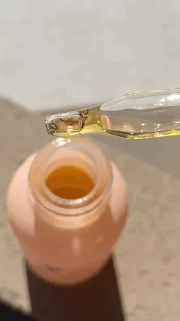 A Brown person applies face oil to her cheek and rubs it in