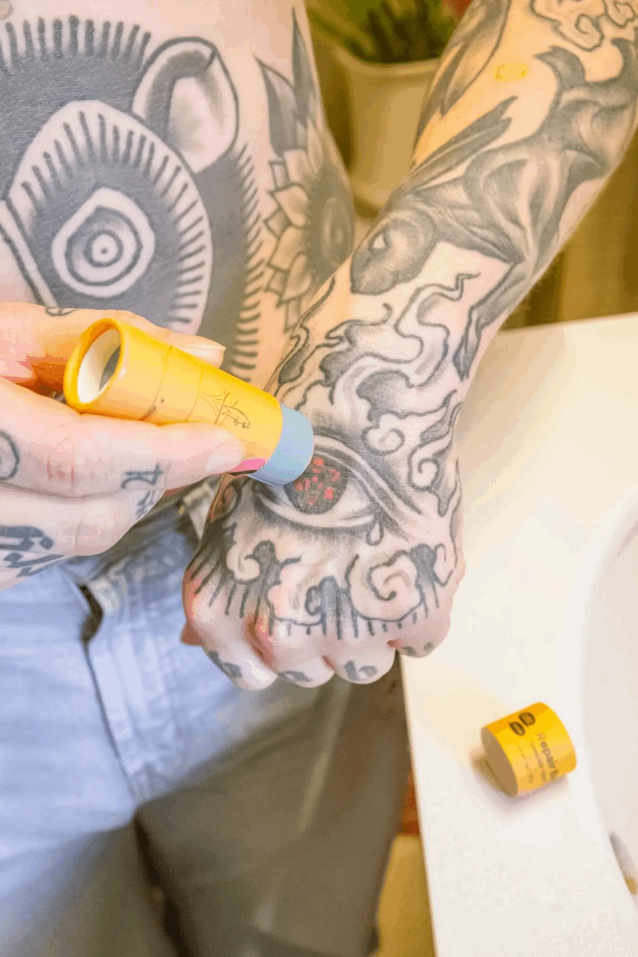 A person with curly hair and lots of tattoos applies repair balm to their tattoos