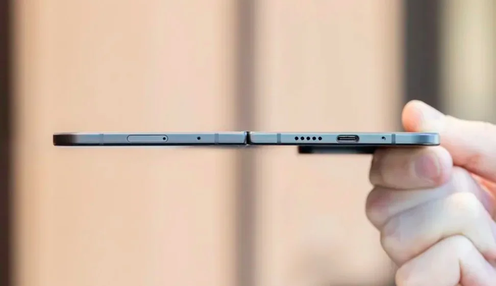 A photo of a hand holding a Pixel 9 Pro Fold open flat and with its profile facing the viewer, showing how thin it is.