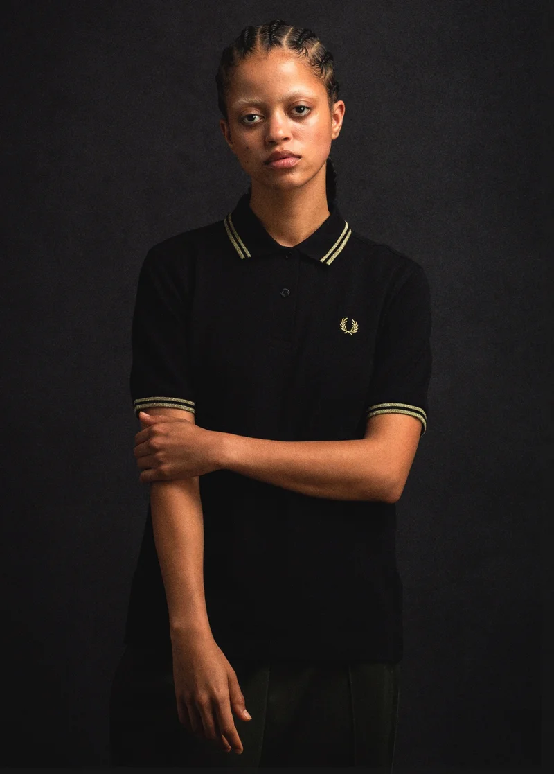 THE LAUNCH OF THE GIFT LIST: Woman wears Black Fred Perry Shirt with Glittery Gold Twin Tipping