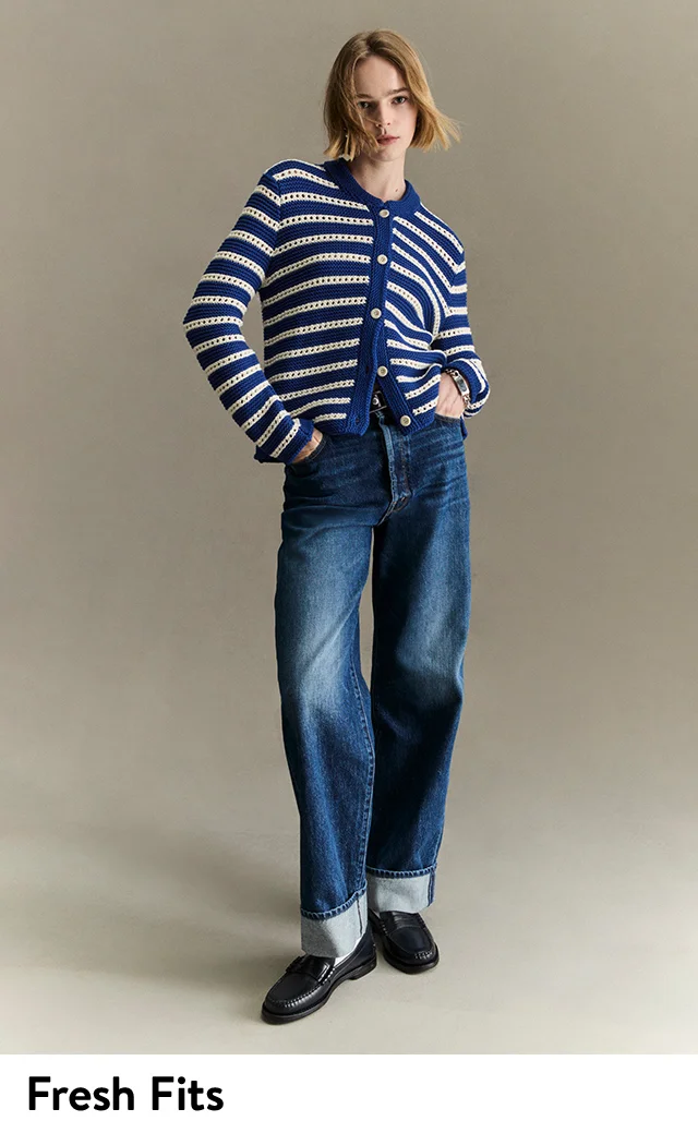 A woman wearing a striped cardigan with jeans and black loafers.