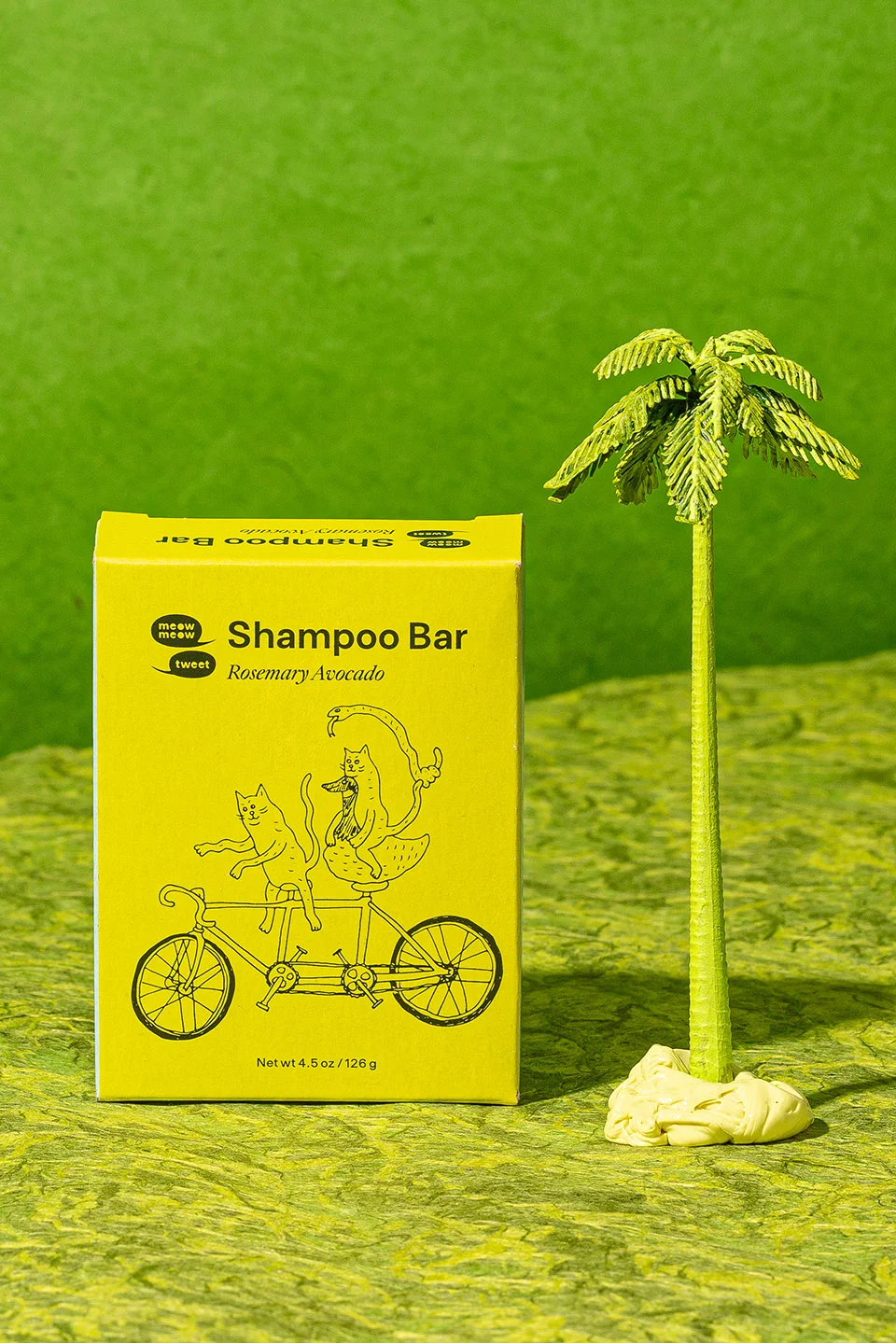 A green box of shampoo next to a toy tree against a green background
