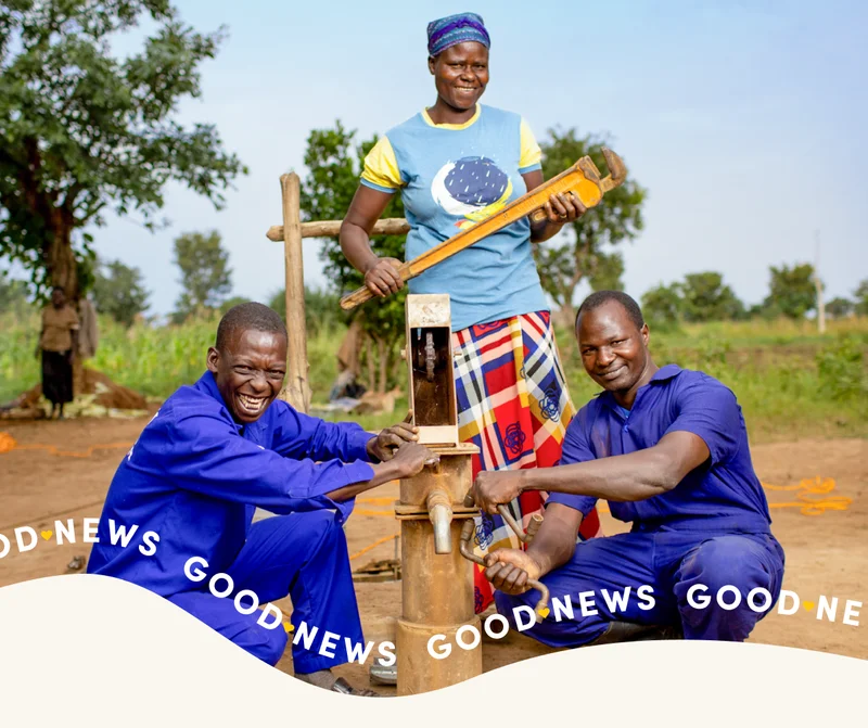 Three men smile at the camera as they install a sensor at a water point.