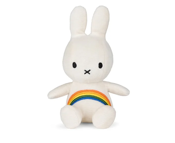 A stuffed white rabbit with a rainbow on its belly sits on a pile of books