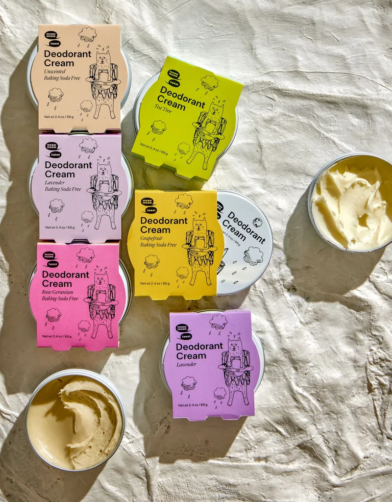 A collection of colorfully packaged tins of deodorant sit on a plaster background