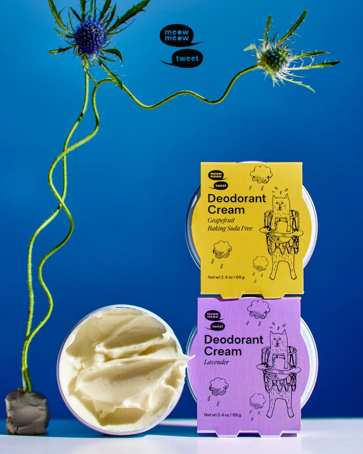 Two speech bubbles with Meow Meow Tweet over an image of three tins of deodorant cream and a spiky flower