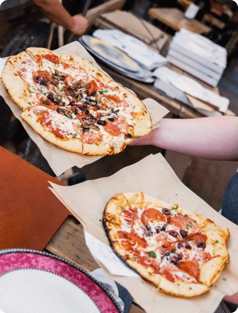 Image Description: A traveler serving two freshly made margherita pizzas sprinkled with olives