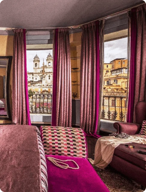 Image Description: Interior of a magenta-accented hotel room with velvet curtains and a suede bedroom bench at The Inn at the Spanish Steps in Rome