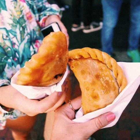 Image Description: A close-up of two travelers toasting with empanadas while on a food tour in Miami