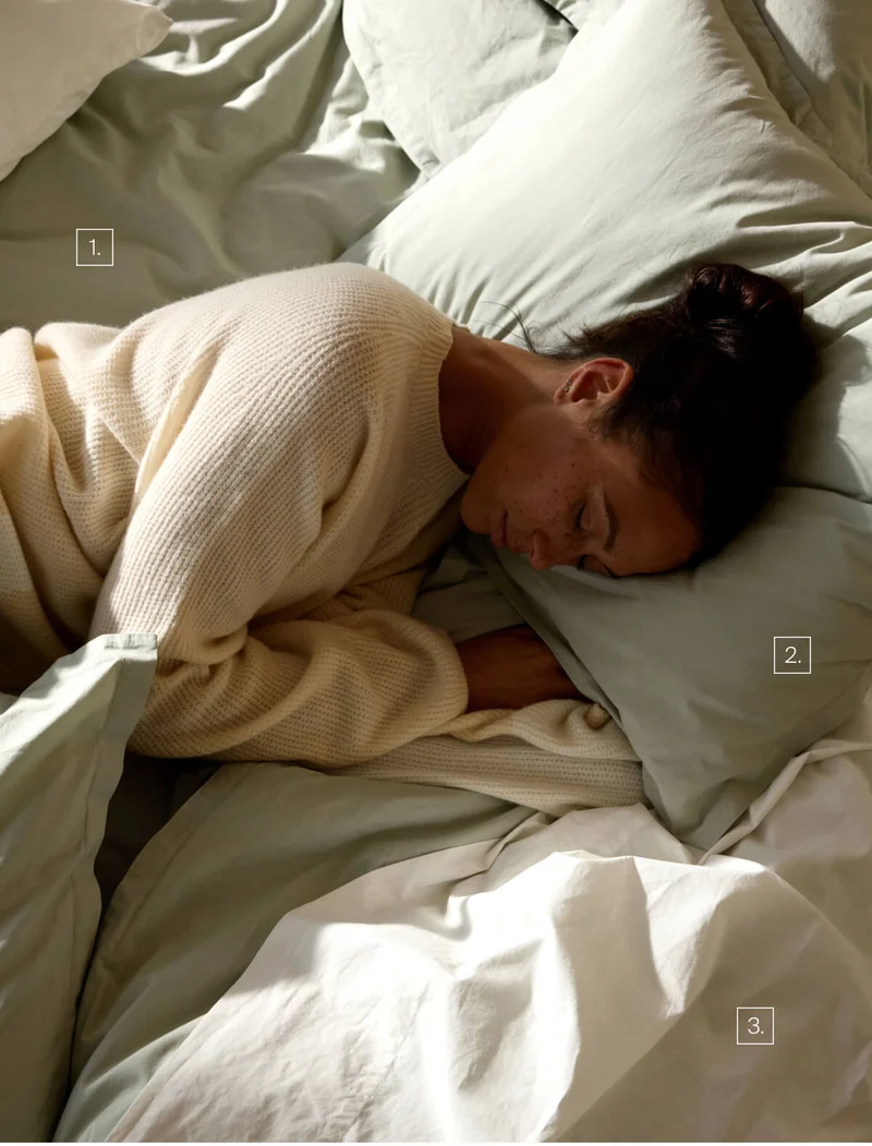 Woman laying in bed with moss duvet cover set and white percale sheeting.