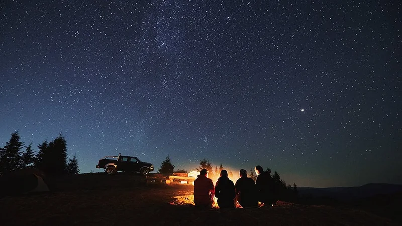 Image description: Hikers sitting near campfire under a starry sky.
