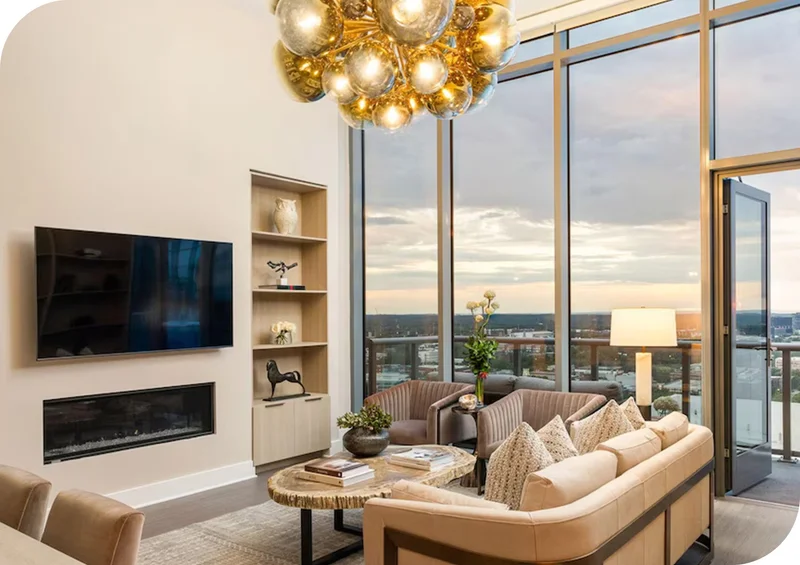 Modern living room with floor‑to‑ceiling windows, warm lighting, and city views at sunset.