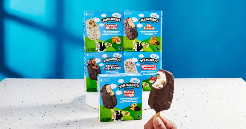 Five packages of new Ben & Jerry's Ice Cream Bars. Hand holding a bar with a bite taken out.