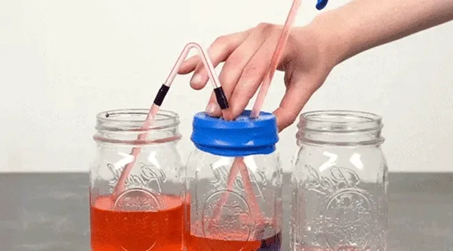 Hands using tubes, jars, and red liquid to demonstrate how a heart pumps blood. Pink GIF label in the corner.