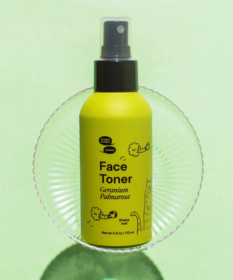 A green bottle of toner is lying down on a green background with a shadow casted.
