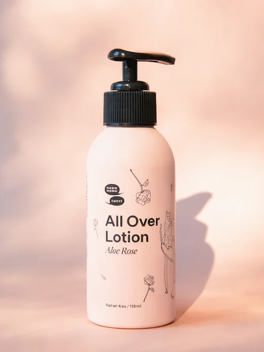 A pink bottle of lotion stands on a pink backdrop with shadows being casted all around.