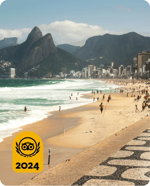 Image Description: People walking on the shore and swimming in the ocean. Mountains and buildings are in the background. A gold Travelers’ Choice Awards Best of the Best 2024 badge is on the bottom left corner.