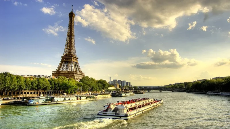 Image description: Eiffel tower and quay Seine river with barges and trees at sunset.