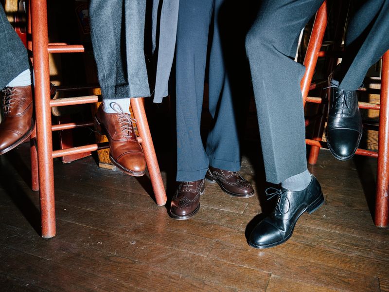 Three GQ staffers wearing men's Oxford shoes while sitting on barstools.