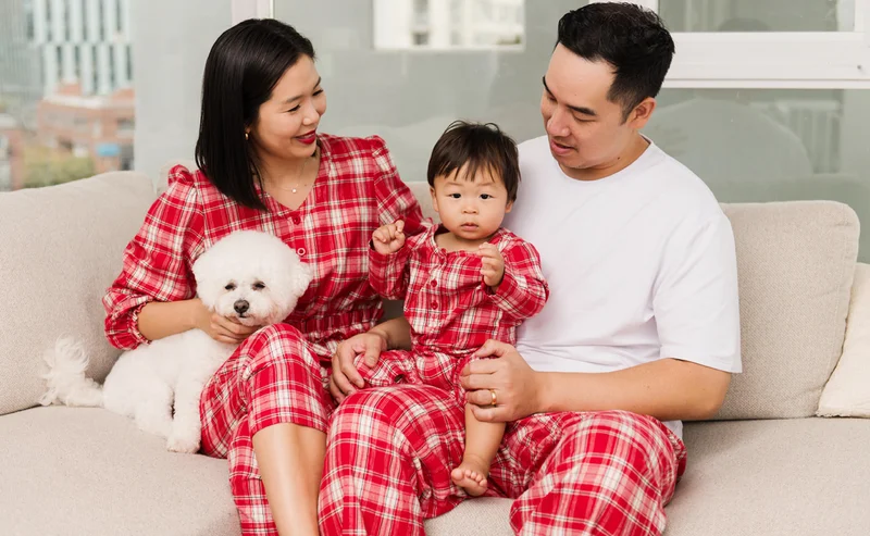 family wearing red plaid rompers with a white dog sat on sofa