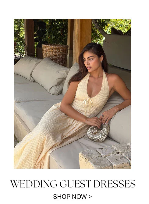 Elegant woman in cream ribbed halter maxi dress, perfect wedding guest attire, with metallic clutch.