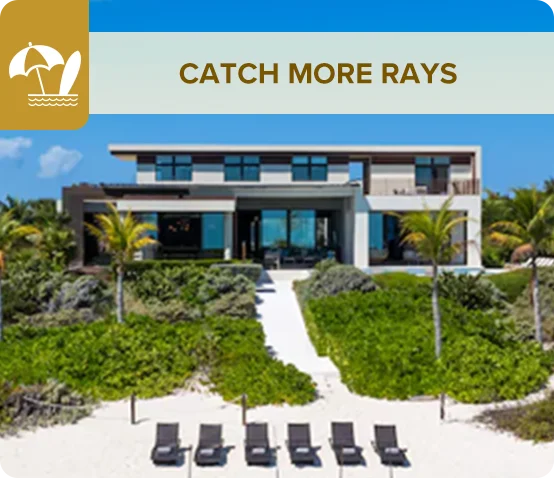 A beachfront villa featuring expansive windows overlooking palm trees and lounge chairs on the white sand.