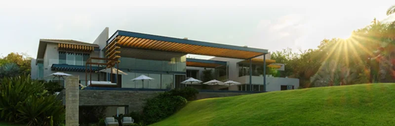 Modern hillside home with shaded terrace and sunlit lawn.