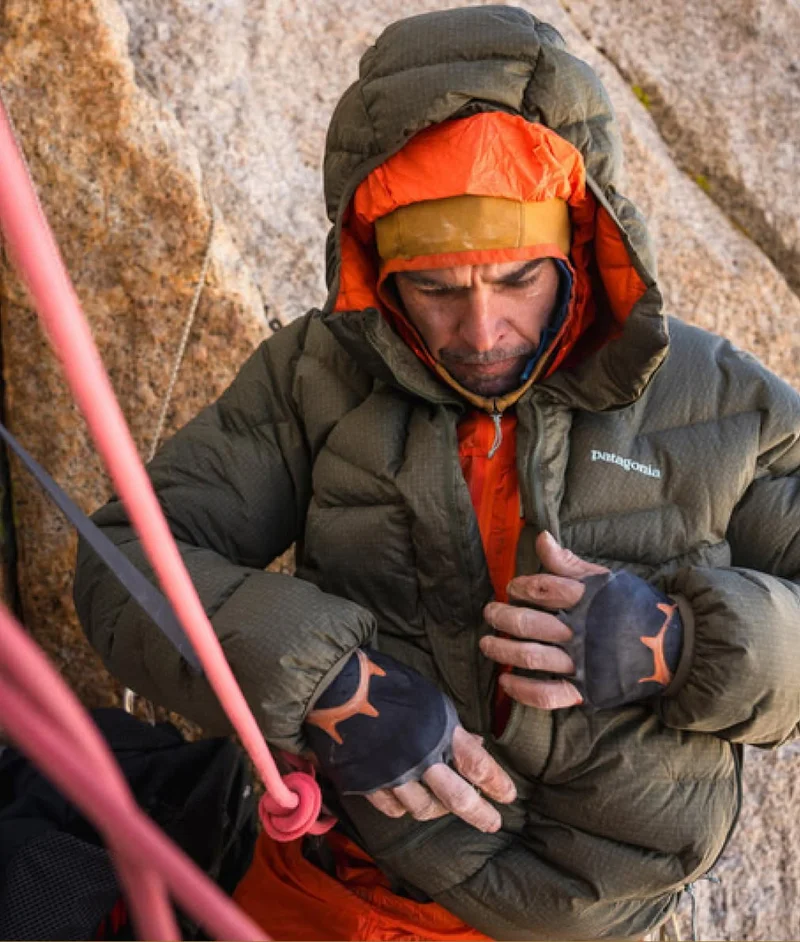 A climber zips up their down jacket in between pitches on a big wall.