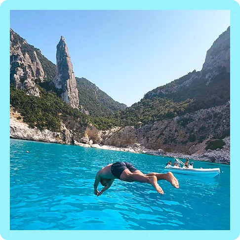 Image description: A person diving into the ocean with a rocky beach and small boat in the background